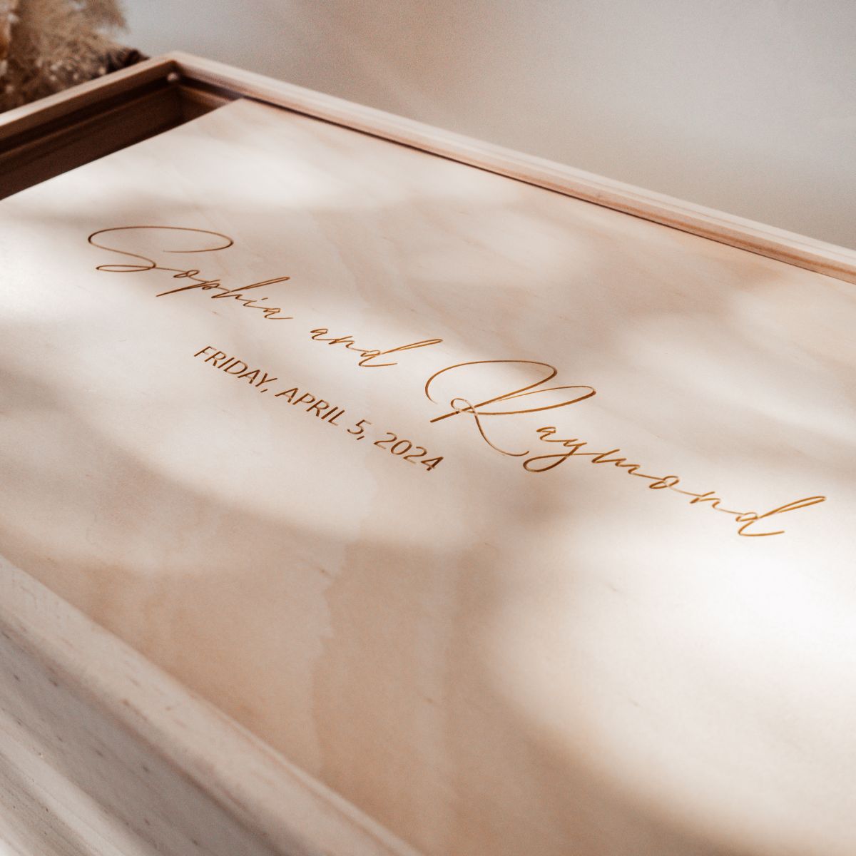 This is a closeup of a large wooden wedding keepsake box with a cursive text design and a date of the wedding underneath